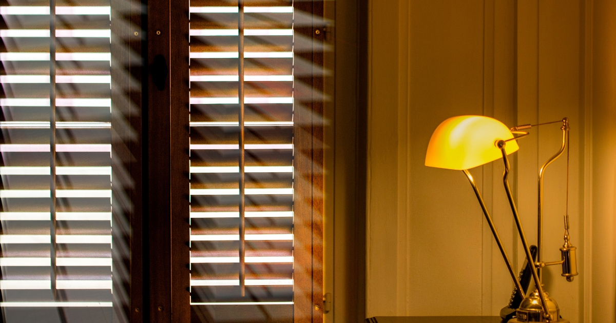 Brown plantation shutters shone by a table lamp